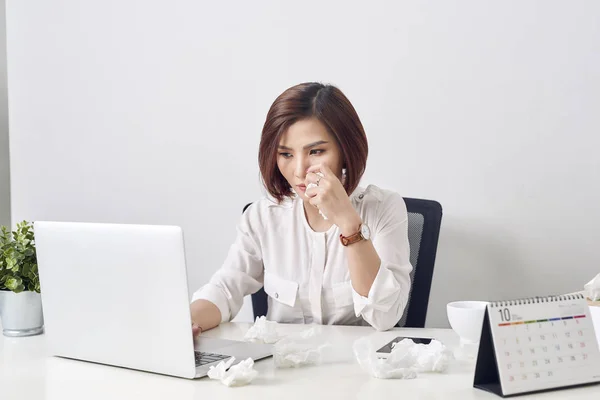 Sad exhausted woman with tissue suffering from cold while working with laptop at table