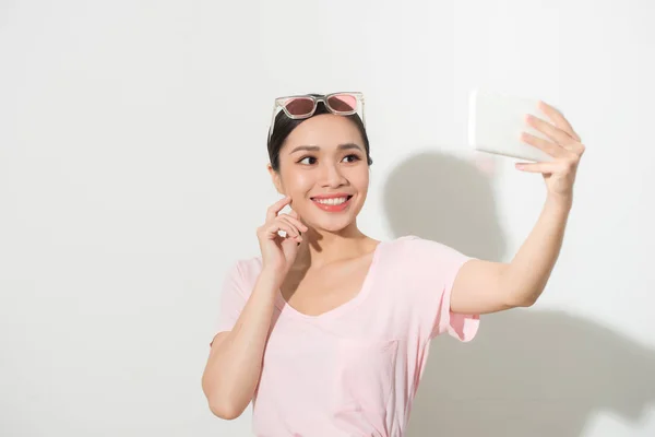 一个年轻迷人的女人用白色背景的智能手机拍自拍照的肖像 — 图库照片