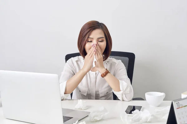 Sad exhausted woman with tissue suffering from cold while working with laptop at table