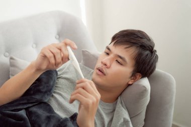 zieke man liggend op de bank gecontroleerd zijn temperatuur thuis in de woonkamer