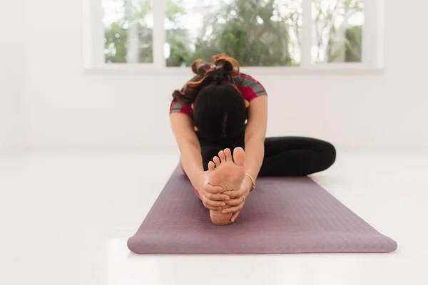 Young attractive yogi woman practicing yoga concept, sitting in Janu Sirsasana exercise, Head to Knee Forward Bend pose, working out wearing black sportswear, full length, white loft studio background