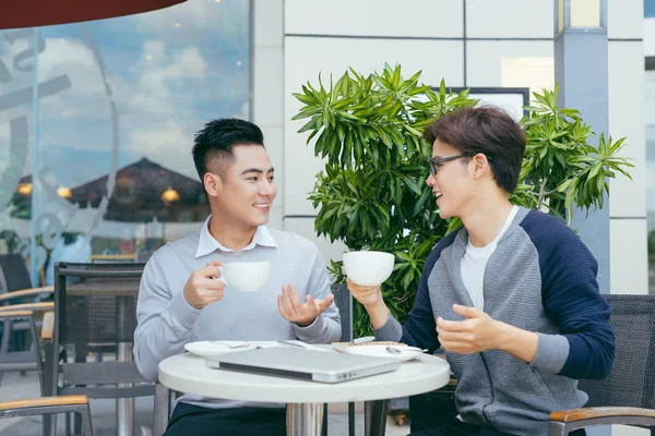 Two young businessmen are chatting in a coffee shop. - Image