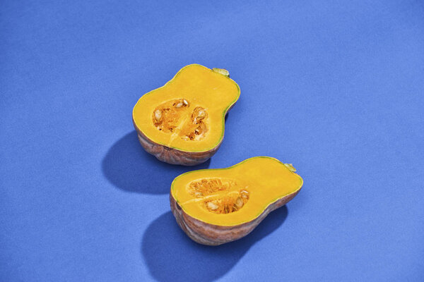 Two halves of ripe butternut squash pumpkin on a blue background. Orange pumpkin with a tail. Close-up