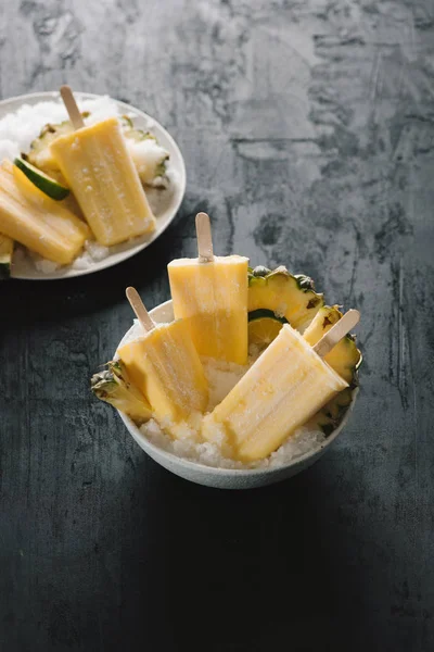 Overhead view of yellow ice lollies inverted in a white bowl on dark table