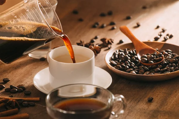 Pouring coffee into cup in middle of accessories on wooden background