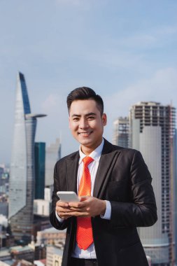 İş adamı arka planda gökdelen binaları olan şehir merkezindeki ofis dışında cep telefonu uygulaması kullanıyor.