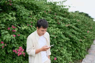 Yakışıklı adam manifatura yeşil parkta yürürken cep telefonunuzda