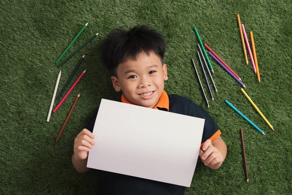 草の上に横たわって公園で描くかわいい7歳の男の子 — ストック写真