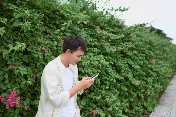 英俊的男人在绿色公园散步时用手机发短信 — 图库照片