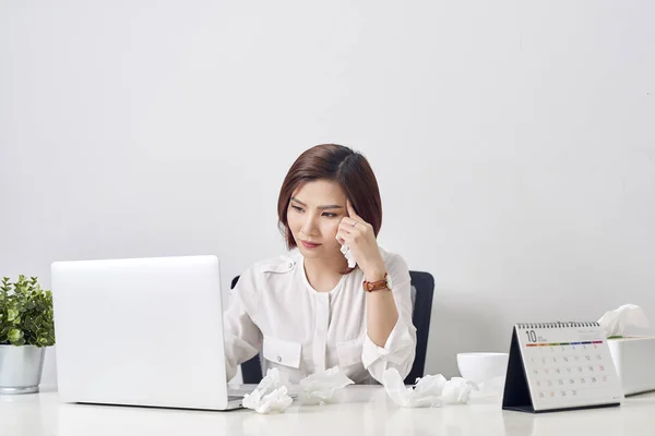 Sad exhausted woman with tissue suffering from cold while working with laptop at table