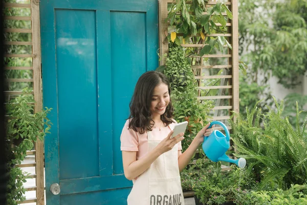 Giardiniere Femminile Utilizzando Cellulare Durante Irrigazione Nel Suo Giardino — Foto Stock