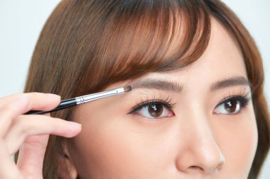 Asyalı genç ve güzel bir kadın kaş üzerine kozmetik pudrası sürüyor, doğal makyaj, güzel yüz.
