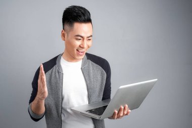 Dizüstü bilgisayar ekranına bakarak ve gri arka plan üzerinde izole kazanmak kutluyor mutlu Asya adam heyecanlı