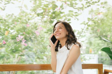 Kafede masada otururken konuşmak, okumak ve mesajlaşmak için akıllı telefon kullanan iş serbest Asyalı kadın.