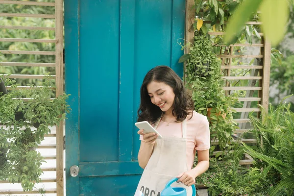 Bahçesini sularken cep telefonu kullanan kadın bahçıvan.