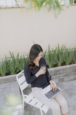 Sabah kahvesini zevk. Çay bardağı tutan ve onun açık evin terasında bir sandalyede otururken kameraya bakarak güzel genç gülümseyen kadın