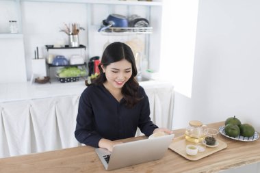 gülümseyen genç kadın mutfakta ev dizüstü kullanarak