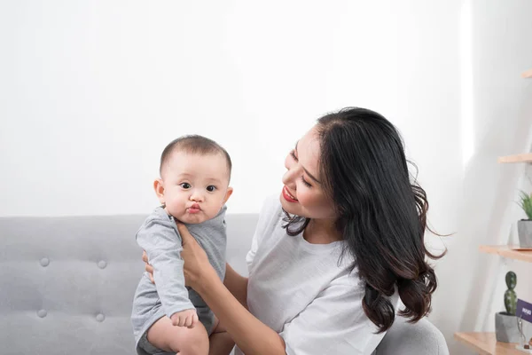 Young mother with her one years old little son dressed in pajamas are relaxing and playing in the living room at the weekend together, lazy morning, warm and cozy scene. Selective focus.