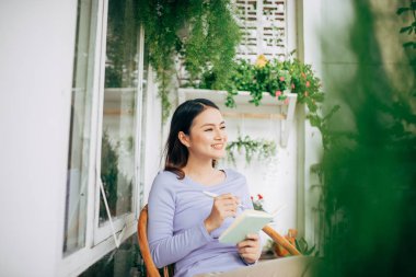 Not defterine yazan kadın beyaz, modern sandalyeye yerleştirilmiş, evde serbest çalışan kadın.