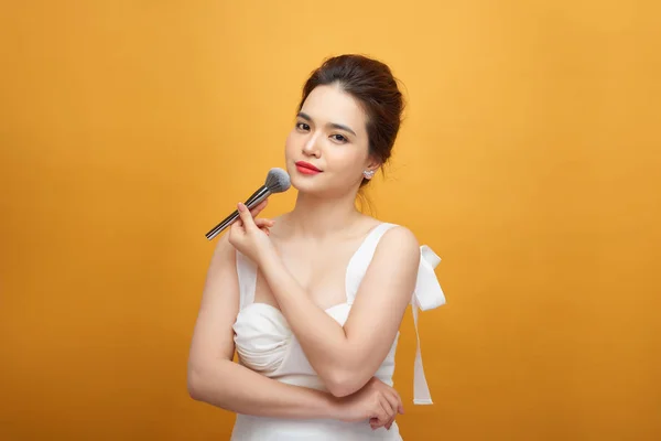 beautiful woman holding makeup brush over yellow