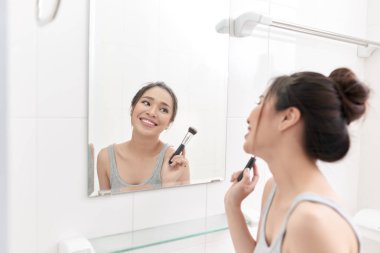 Genç bir kadın banyo aynası önünde duran ve makyaj.