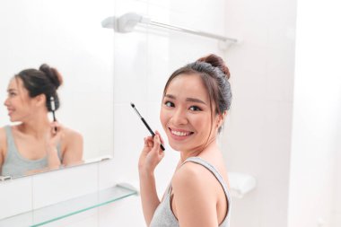 Genç bir kadın banyo aynası önünde duran ve makyaj.