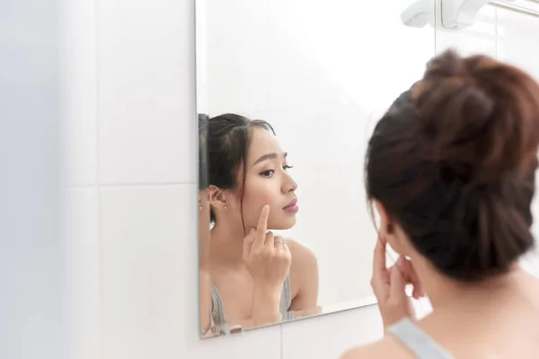 Skin care. Woman applying skin cream on her face in front of mirror