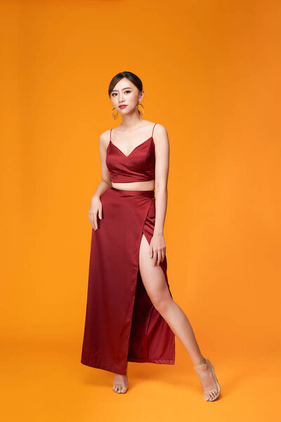 Full length portrait of young sexy woman in red dress  standing and posing against yellow background