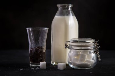 Bir şişe süt, bir bardak kabarcık ve siyah masada bir şeker pot