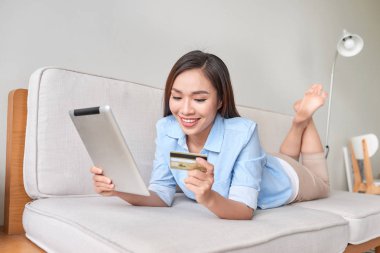 mutlu kadın oturma odasında kredi kartı ile online alışveriş için dijital tablet kullanma