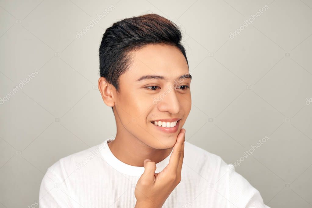 Portrait of shirtless young handsome Asian man checking his face for skin care and beauty concepts on white background