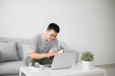 Yakışıklı Genç Adam Oturma Odası Kanepede Oturan, Onun Laptop Bilgisayar bakarken bazı notlar yazma