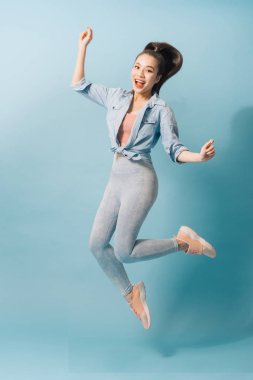 Neşeli bir genç kadın tam uzunlukta portre atlama ve açık mavi arka plan üzerinde kutluyor