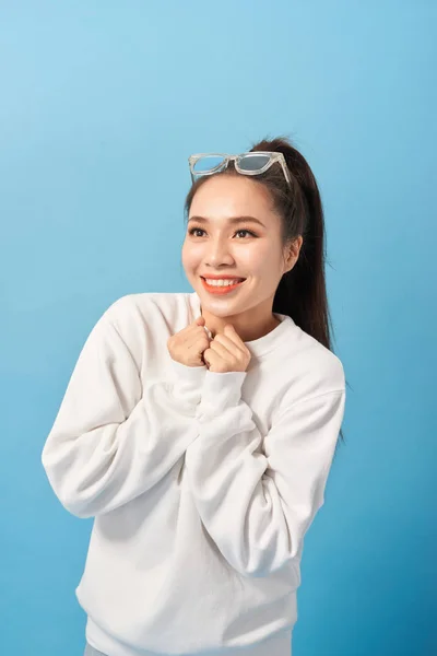 Happy woman keeps hands under chin looks joyfully at camera, notices something very pleasant, isolated over light blue background