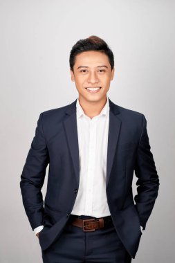 Takım elbiseli Genç bir Asyalı adam pantolonu cebinde, beyaz bir arka planda izole her iki elini koydu.
