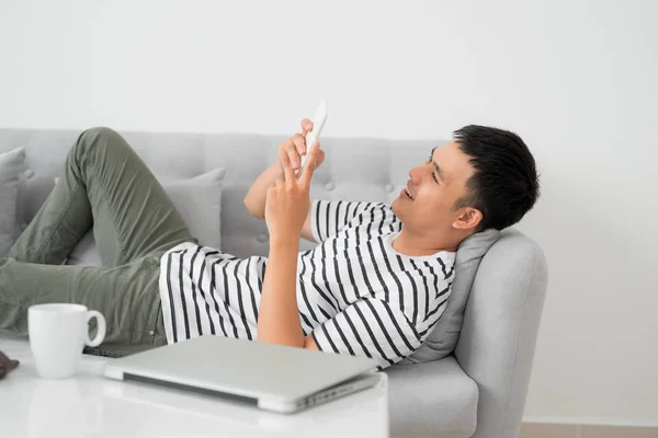 Asian young man using mobile phone while lying indoor.
