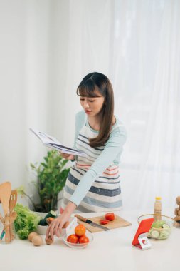 Mutfakta yemek kitabı okuyan genç bir kadın yemek tarifi arıyor.
