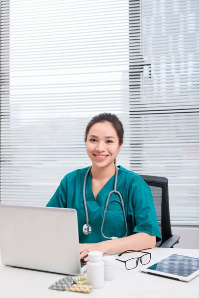 Female doctor working at office desk and smiling at camera, office interior