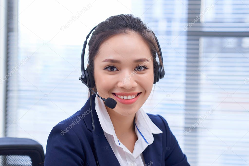 Portrait of happy smiling female customer support phone operator at workplace. Asian 