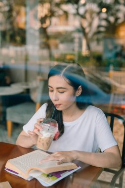 Kafede masada oturan ve kitap okuma genç güzel kadın resim.