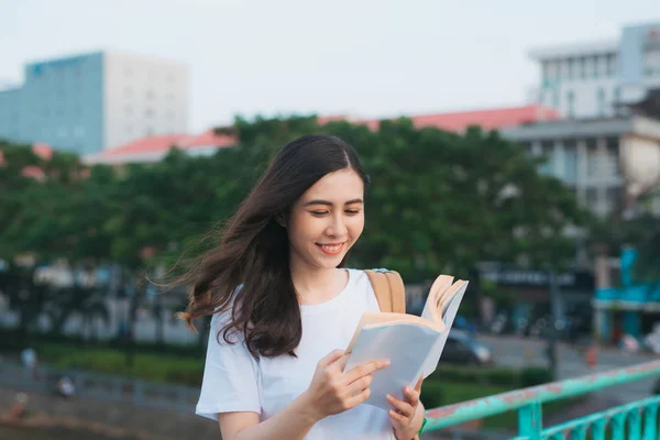 美しいベトナムの女の子の肖像画立って ぼやけた都市の背景と風の中で本を読んで 大学で幸せな読者 — ストック写真