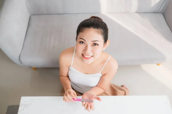Attractive Asian woman correcting fingernail using nail fail, sitting at table