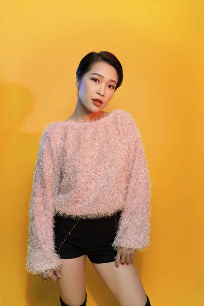 Inspired asian young woman dancing in studio and laughing. Pretty girl in cute dress jumping on yellow background.