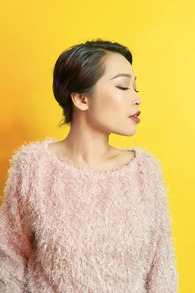 Adorable woman expressing true positive emotions during photoshoot in pink fur coat. Indoor portrait of active glamorous girl standing in confident pose and smiling.