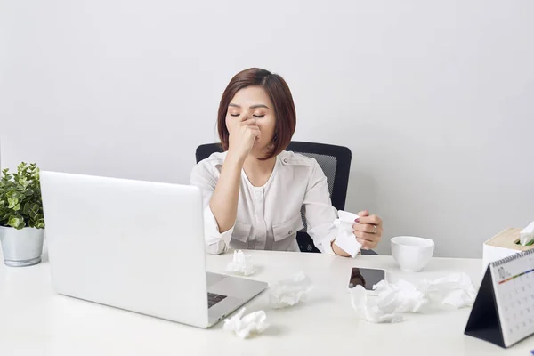 Sad exhausted woman with tissue suffering from cold while working with laptop at table