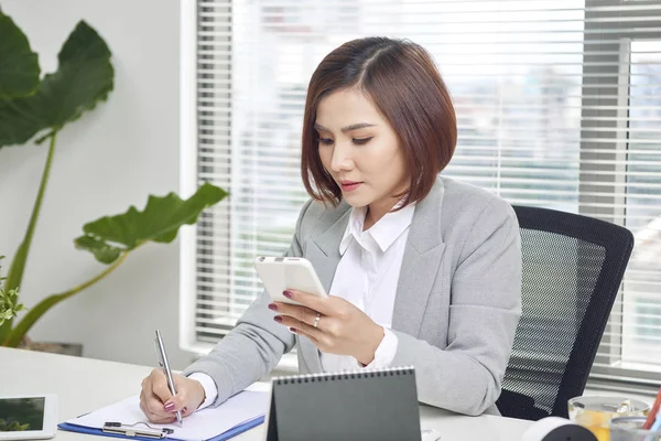 Empresaria Tomando Notas Mirando Celular Oficina Mujer Empresaria Sentada Mesa — Foto de Stock