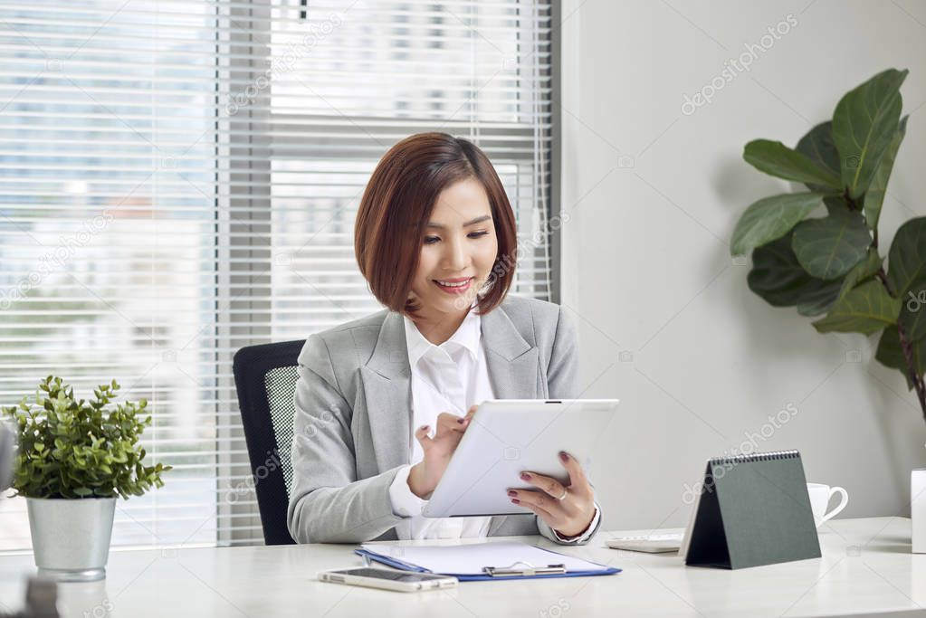 Asian businesswoman working with tablet computer at office desk.