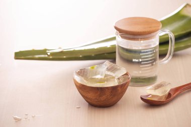 Ahşap arka plan üzerinde soyulmuş aloe vera ve yeşil yaprakları ile Kase