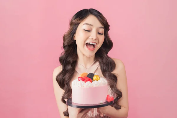 Joyful woman with cake front pink background