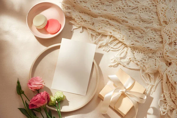 Açık arka plan üzerinde boş not, kraft zarf, hediye kutusu, kumaş ve çiçekler üst görünümü